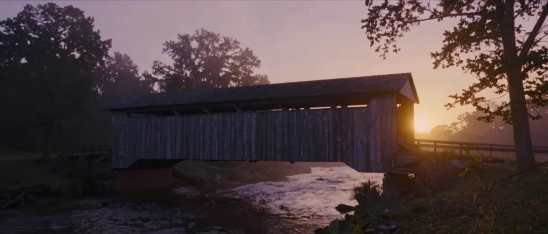 A covered bridge over a creek at dawn.