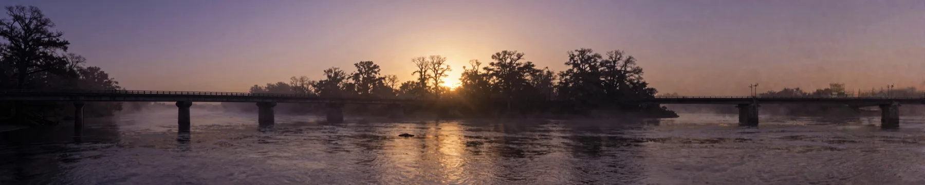 A two-lane bridge crossing a river at dawn.