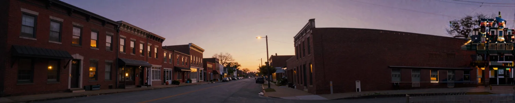 A row of brick buildings at dusk, windows starting to glow.